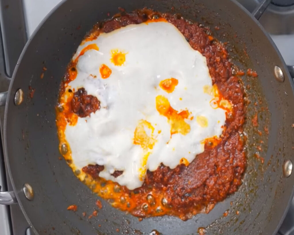 Curd being mixed into tomato gravy for creamy paneer butter masala