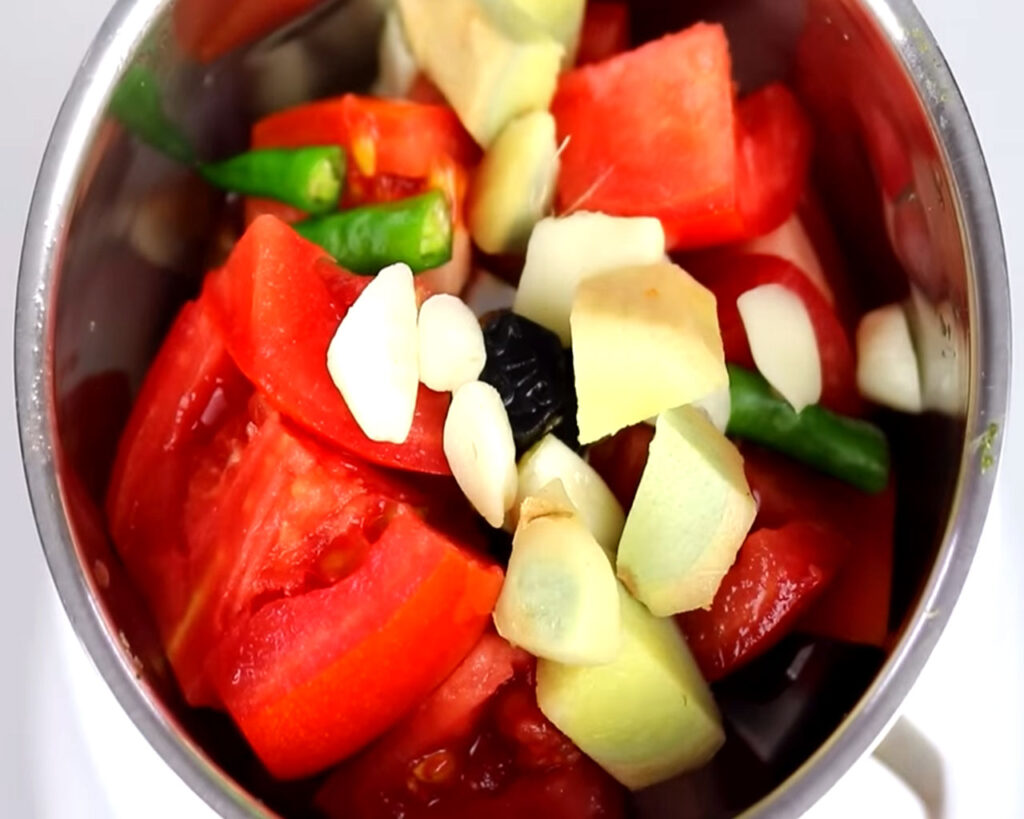 Blender jar filled with chopped tomatoes, ginger, garlic, and green chilies being blended into a smooth paste for restaurant-style bhindi masala