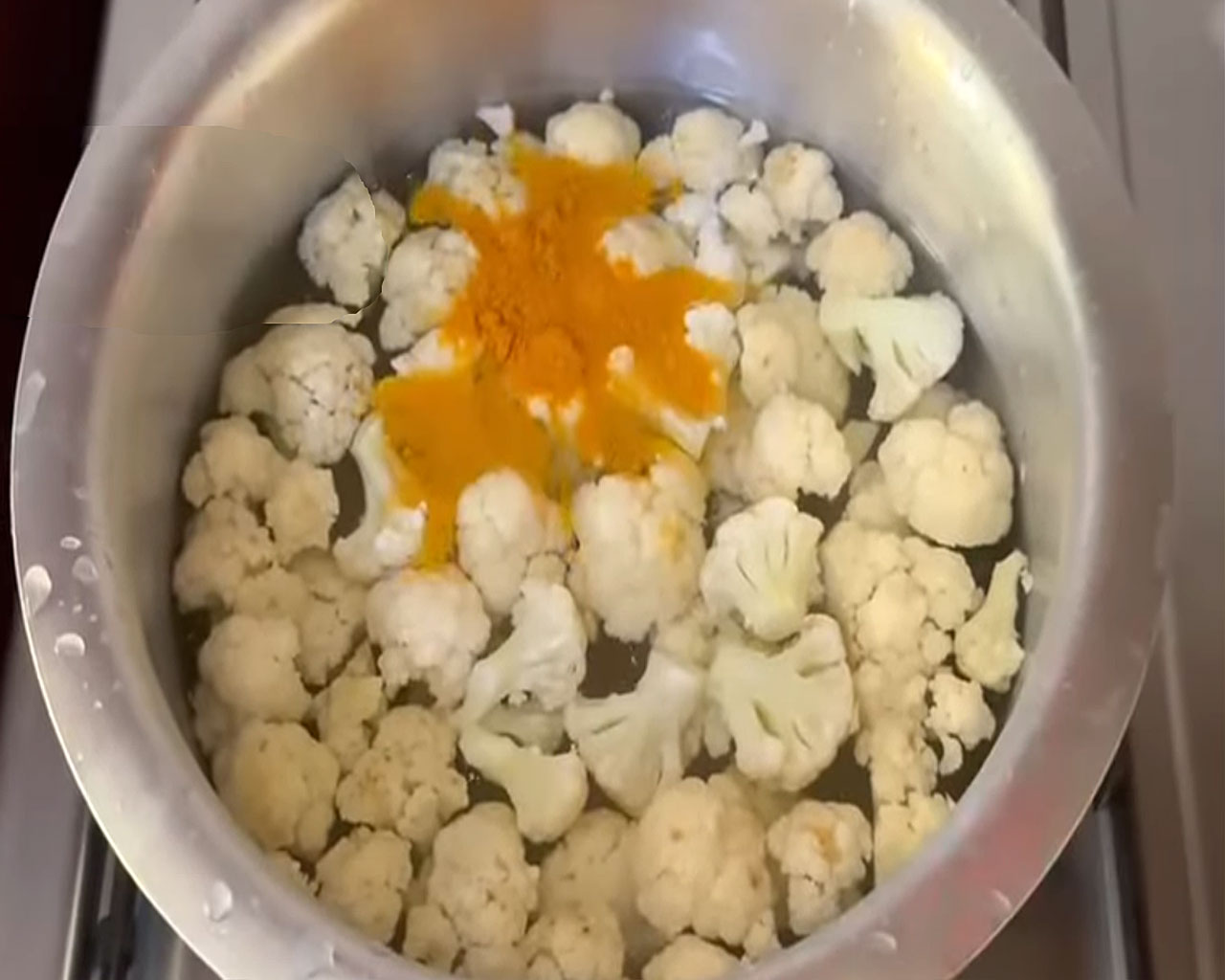 Cauliflower florets boiling in a saucepan with turmeric and salt.