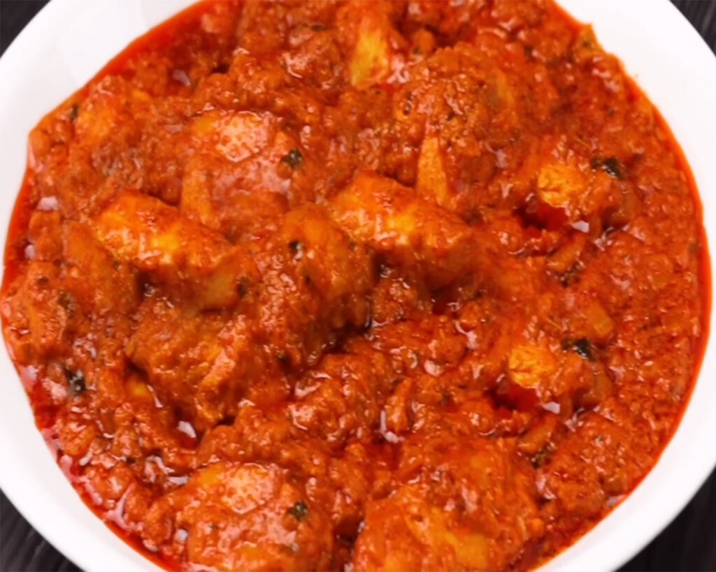 Chicken Tikka Masala being transferred to a plate, ready for garnishing with fresh cream and coriander leaves