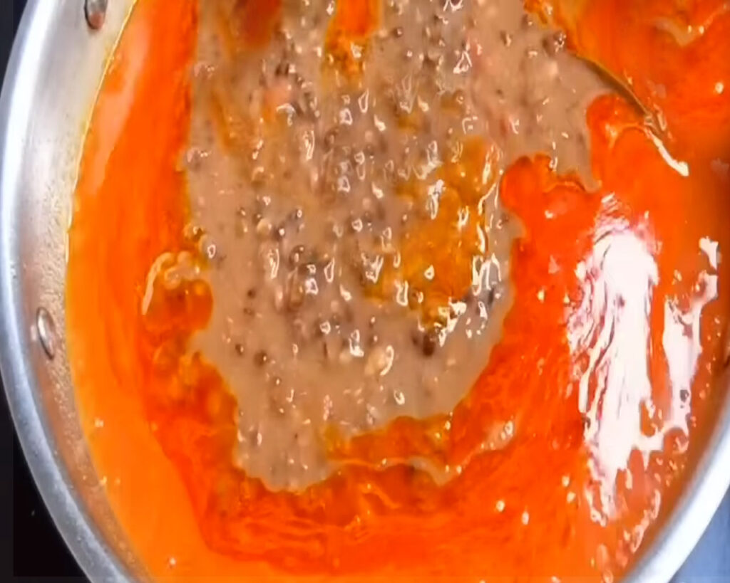 Mashed Dal Makhani being mixed into the tomato gravy in a pan.