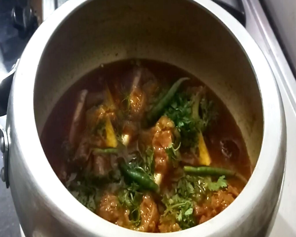Cooked Rogan Josh garnished with garam masala, cumin powder, and fresh coriander leaves in a cooker, ready to serve.