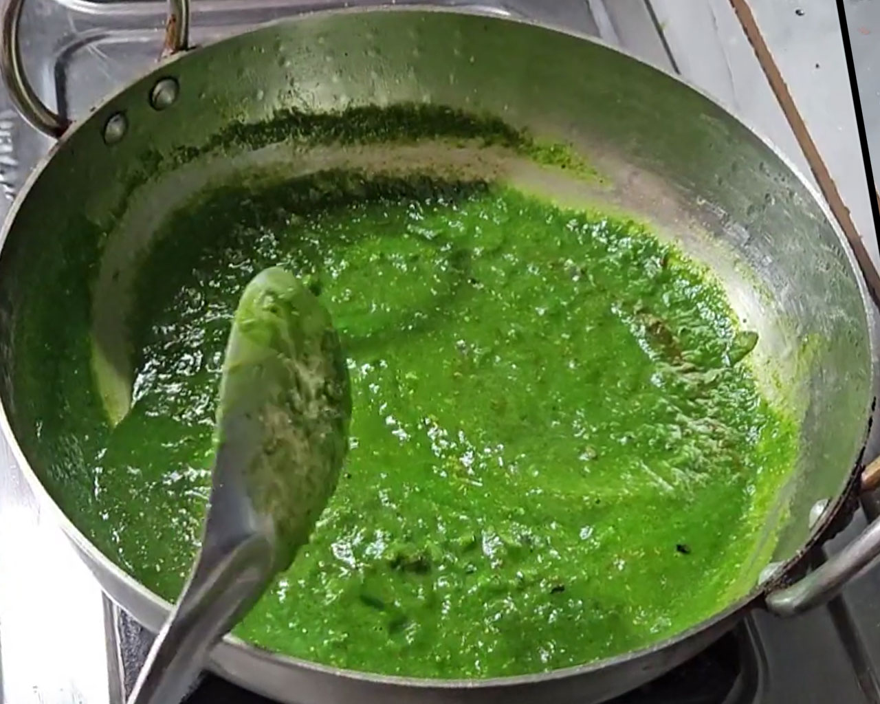 Green spinach gravy with red chili and coriander powder cooking on medium flame