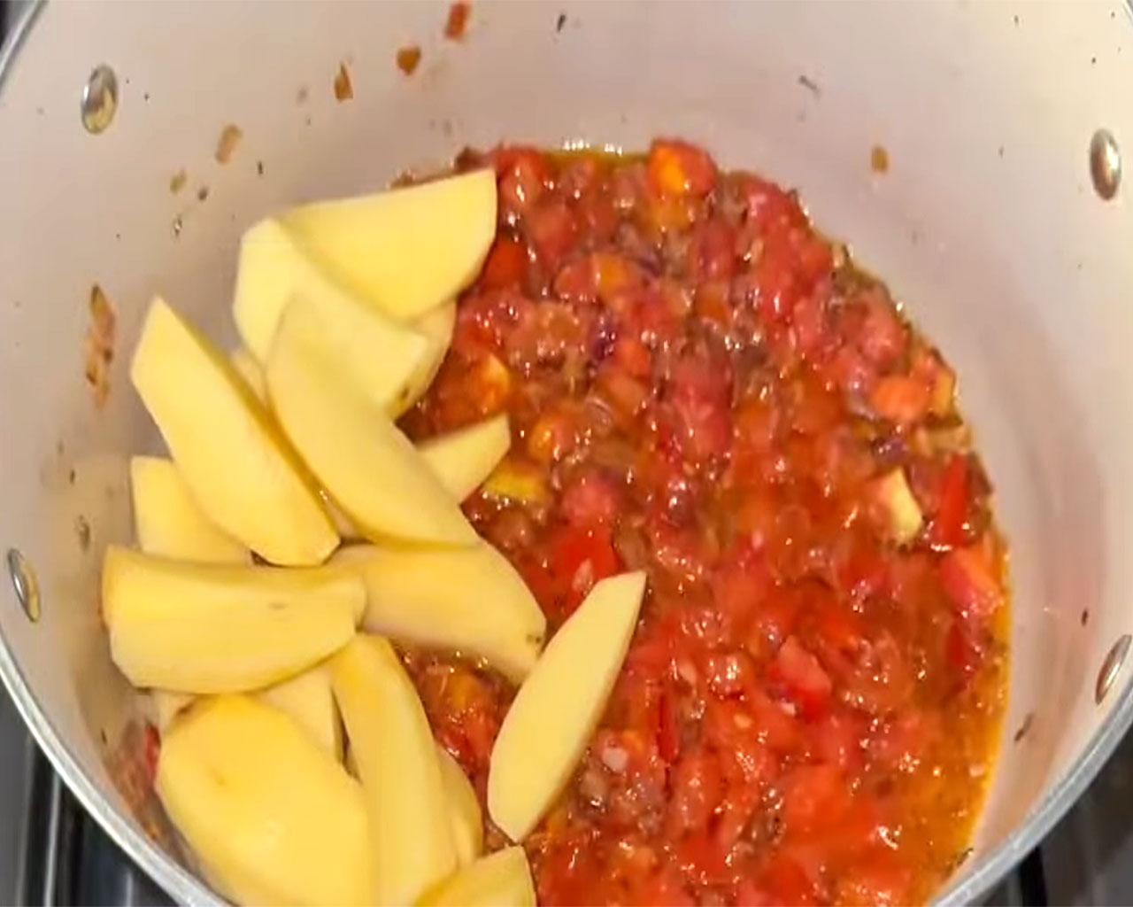 Potato cubes being added to tomato-onion gravy