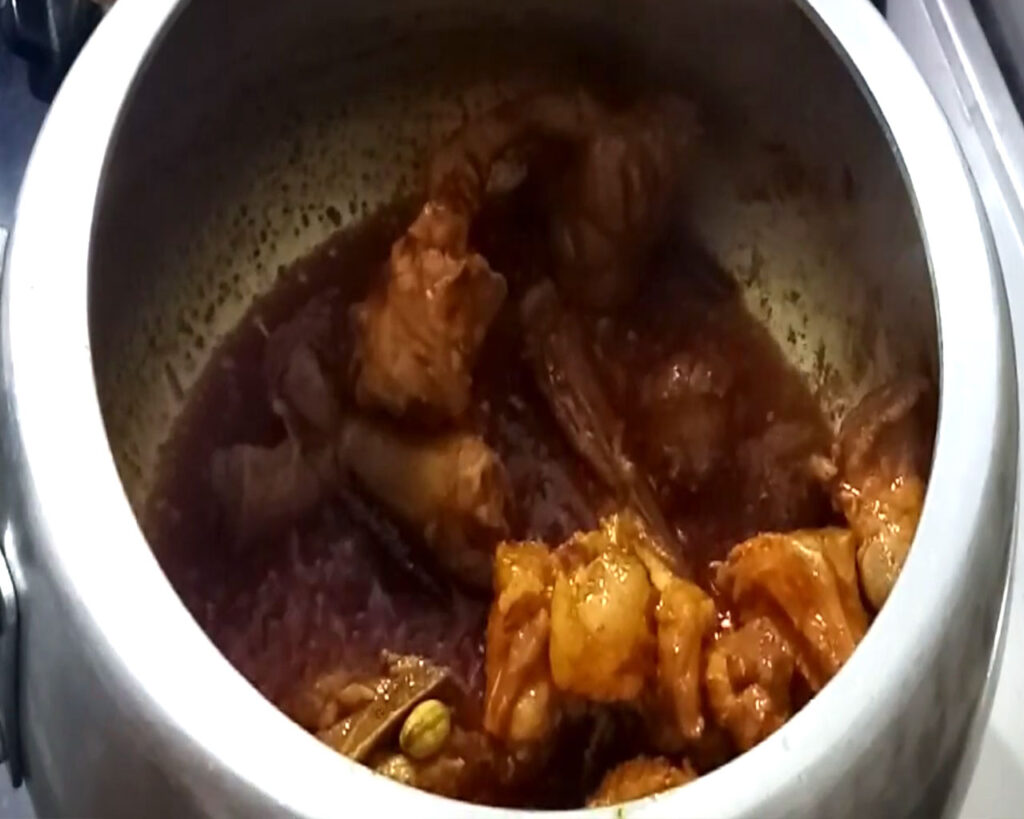 Mutton coated with vibrant Kashmiri red chilli powder, turmeric, and salt, being mixed with a splash of water.