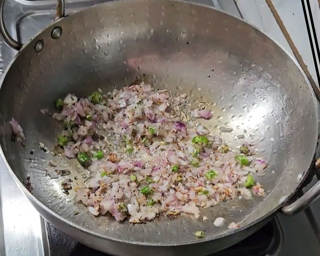 Chopped onions, green chilies, and mustard seeds being sautéed in a wok for Palak Paneer