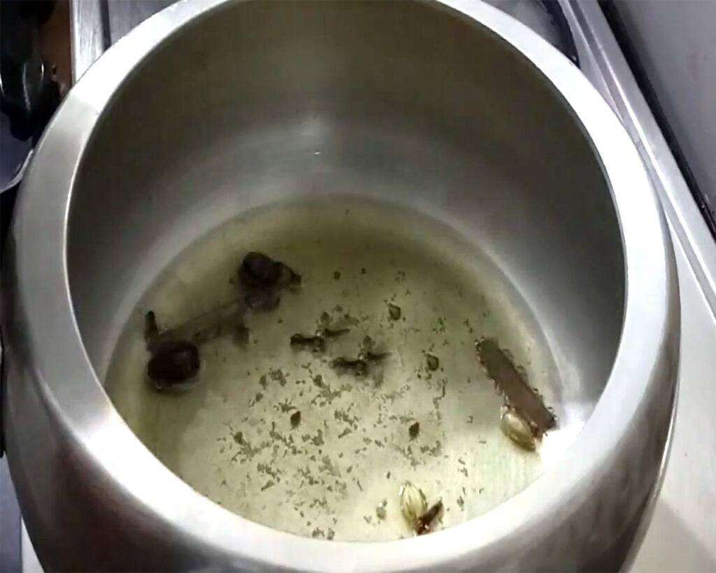 Aromatic whole spices like cloves, cardamoms, cinnamon, and asafoetida frying in hot ghee inside a cooker.