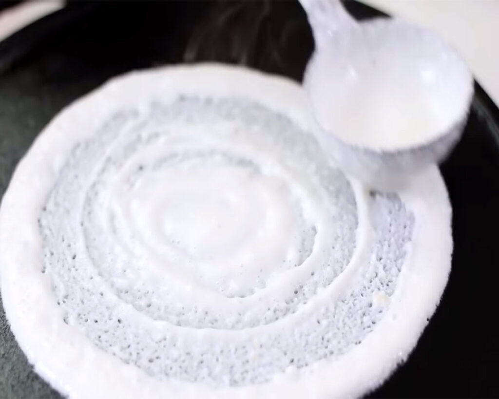 Spreading dosa batter in a circular motion on the tawa to form a thin, even layer for crispy dosas.