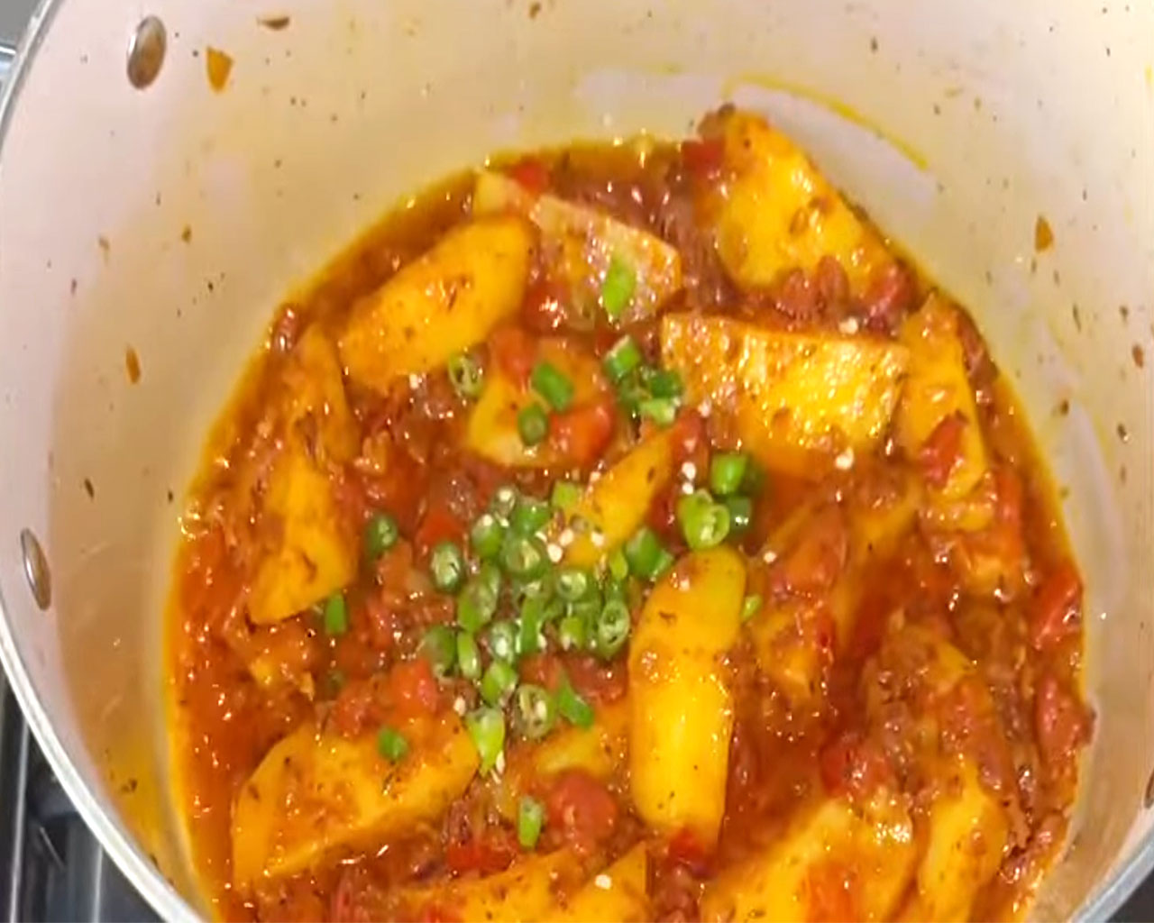 Spices and green chilies being mixed into the spicy gravy