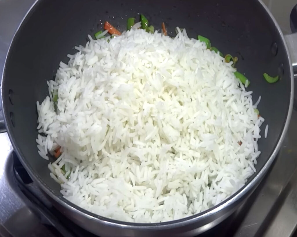 Rice added to stir-fried vegetables in wok for Veg Fried Rice