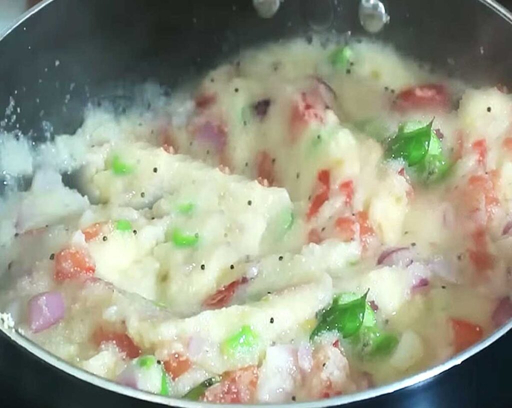Slowly pouring boiling water into roasted rava while stirring for lump-free upma.
