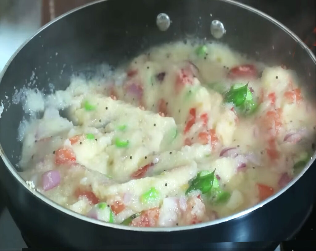 Slowly pouring boiling water into roasted rava while stirring for lump-free upma