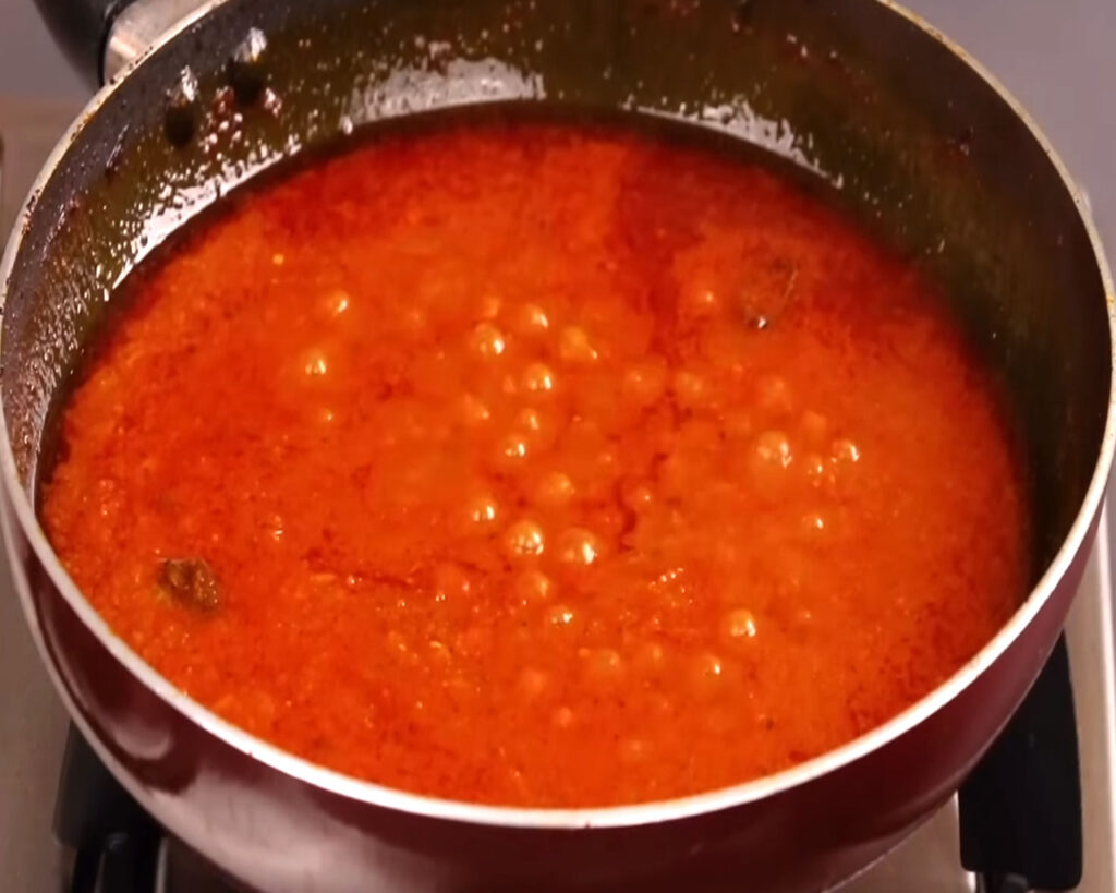 Tomato-based gravy simmering in a covered pan on medium-low flame, getting ready for adding chicken pieces