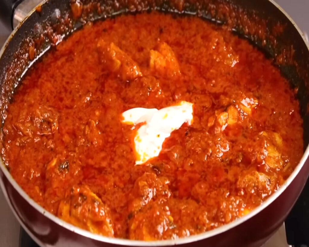 Fresh cream added on top of chicken tikka in gravy, being mixed before covering the pan to cook