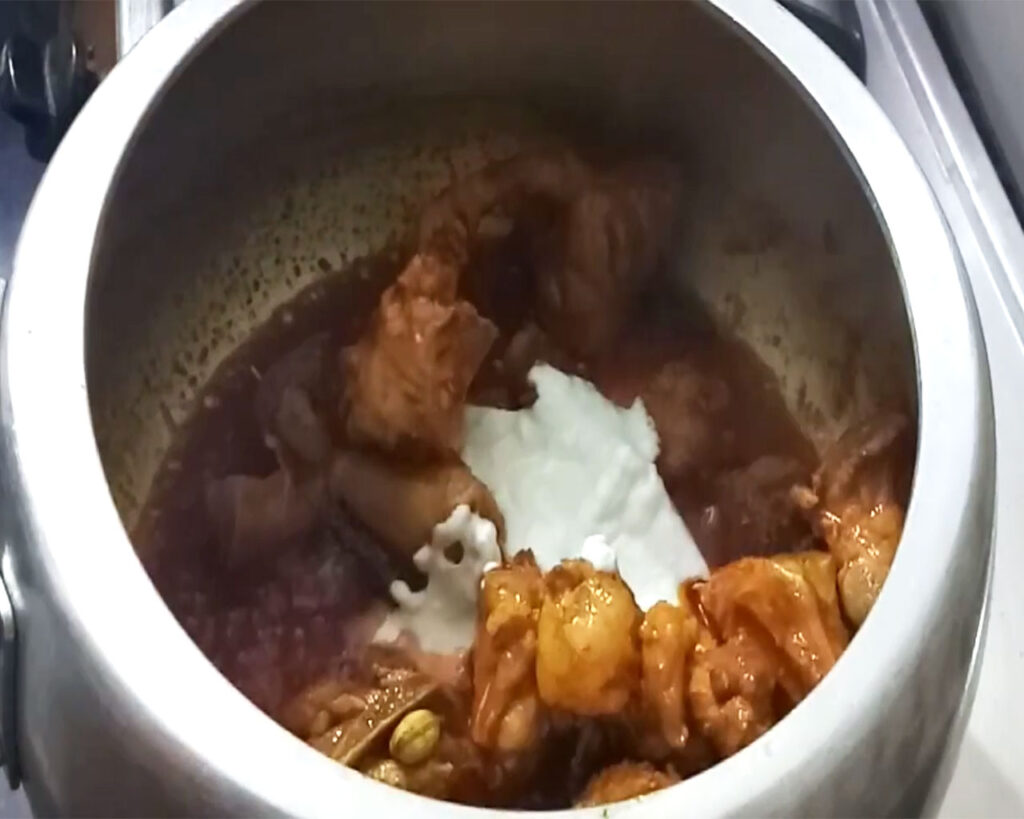 Thick curd being stirred into spicy mutton curry in the cooker, blending to form a rich gravy for rogan josh recipe
