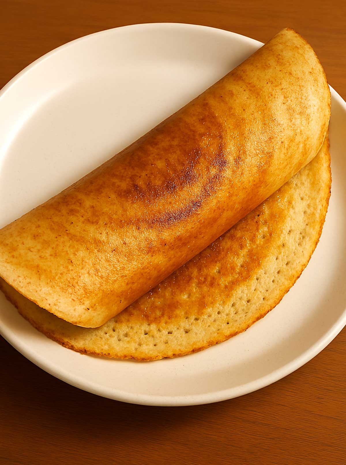 A golden-brown, thin and crispy dosa served on a white plate, highlighting an authentic Indian breakfast experience.