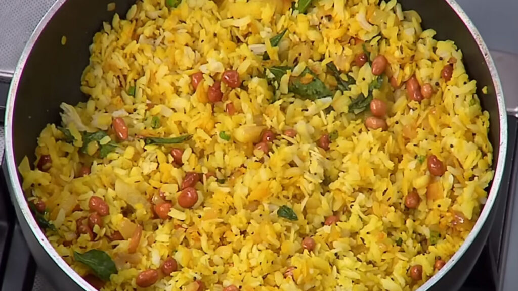 Kanda Poha is ready to serve, yellow poha with onions, peanuts, coriander, lemon, and sev on top
