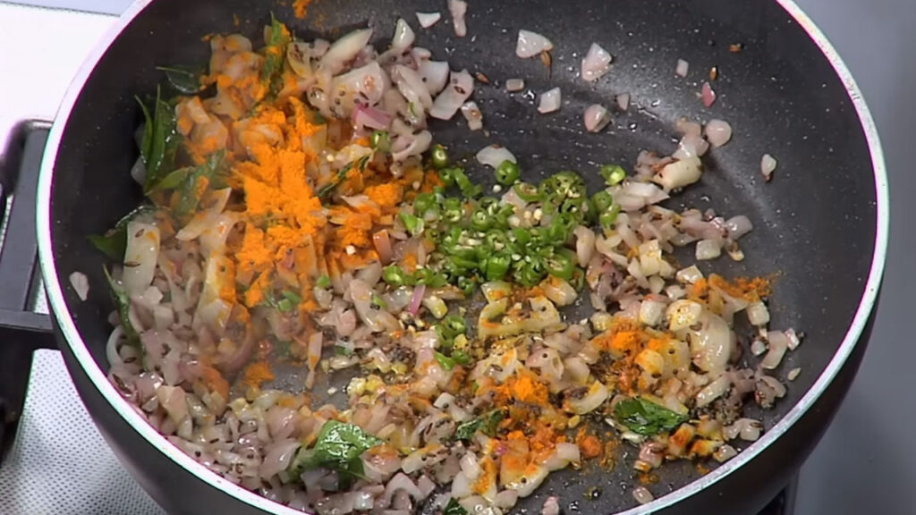 Tempering mustard seeds, curry leaves, green chilies, and onions in oil for Kanda Poha