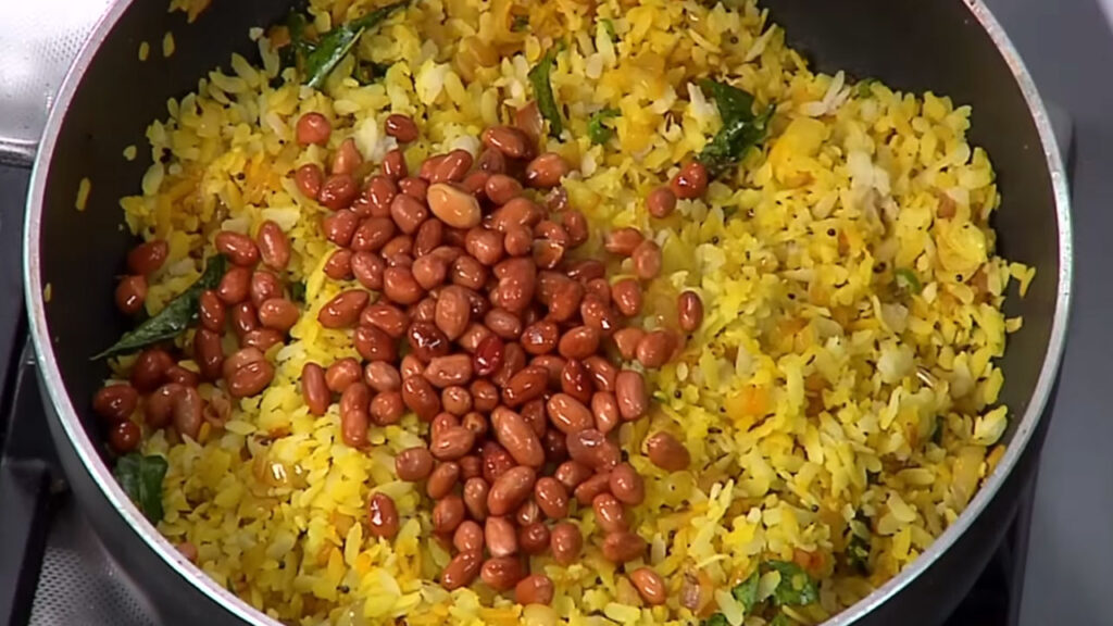 Kanda Poha garnished with roasted peanuts, fresh coriander, lemon wedge, and sev for a crunchy finish