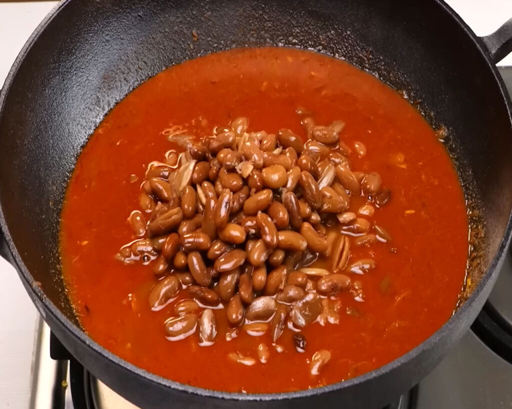 Boiled kidney beans being mixed with spicy onion-tomato masala in a pan for final simmer.