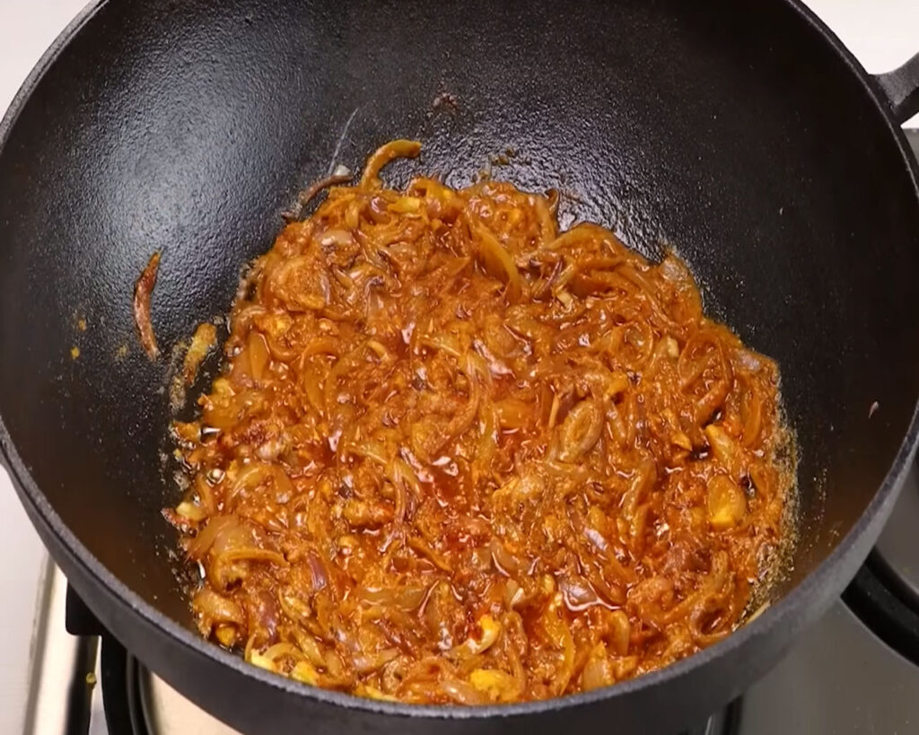 Mixing turmeric, cumin, coriander, and Kashmiri chili powder into sautéed onions to build flavor.