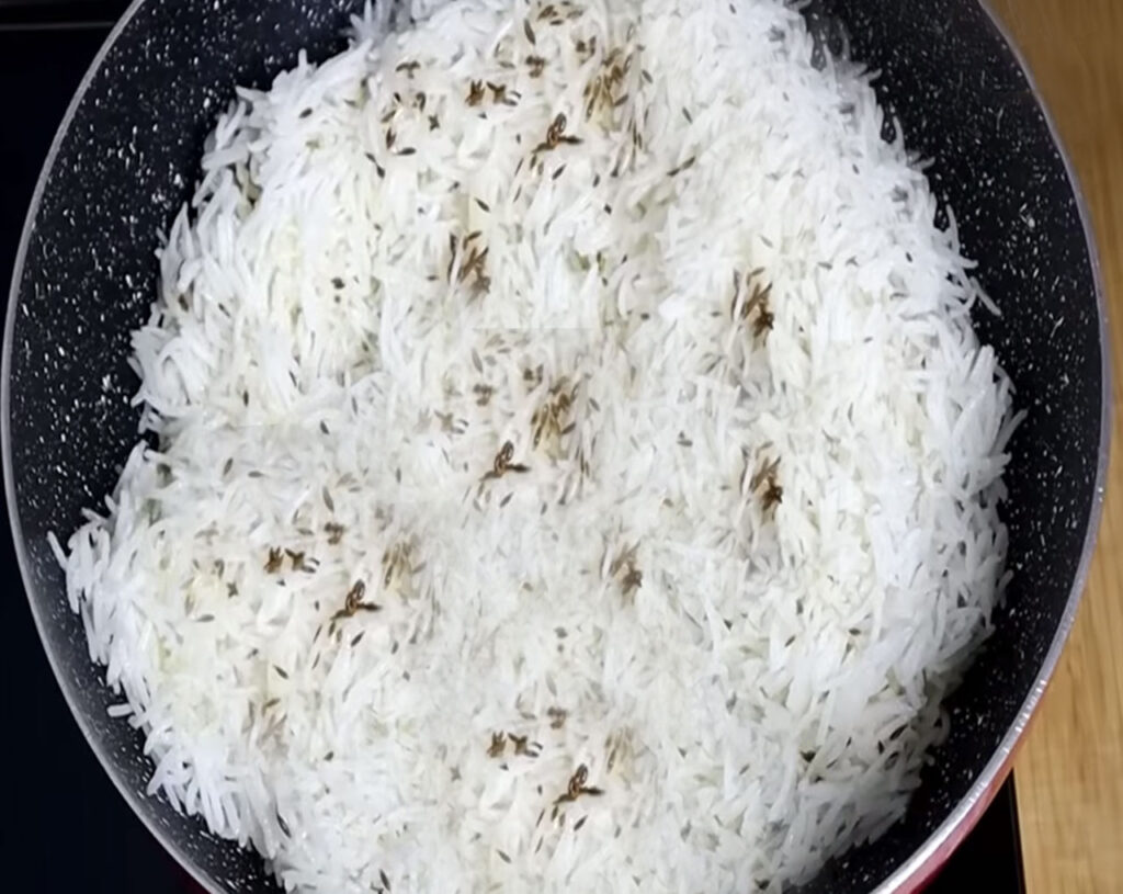 Fluffy jeera rice being fluffed with a fork after cooking
