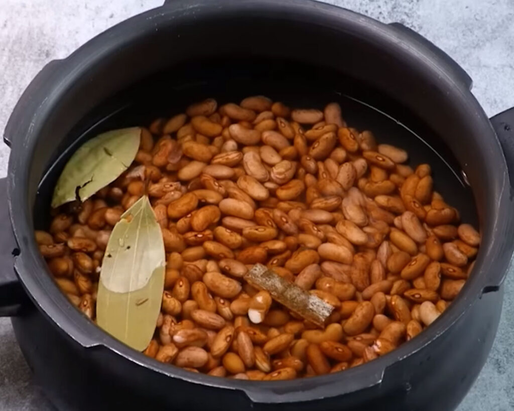 Soaked rajma being pressure cooked with whole spices like bay leaves, cinnamon, and cardamom.