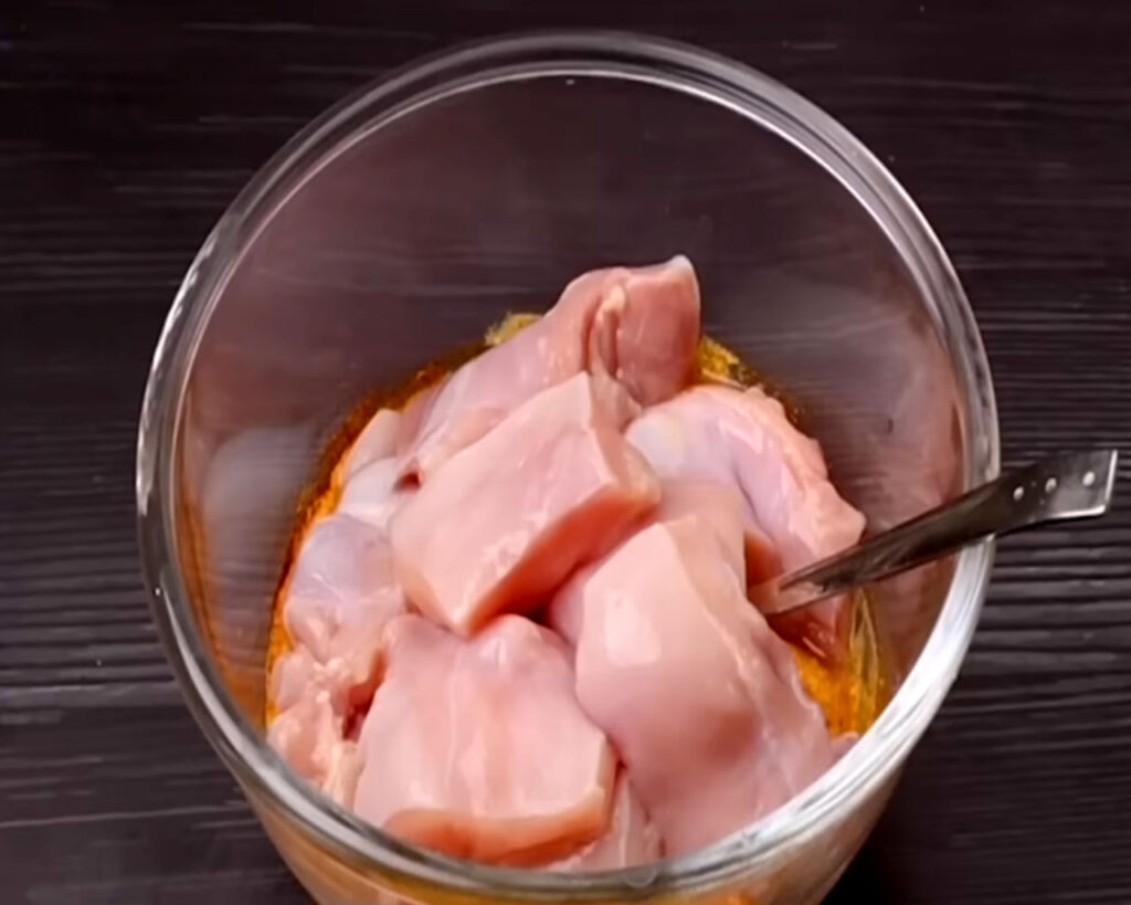 Raw chicken cubes added to a bowl of spiced yogurt marinade