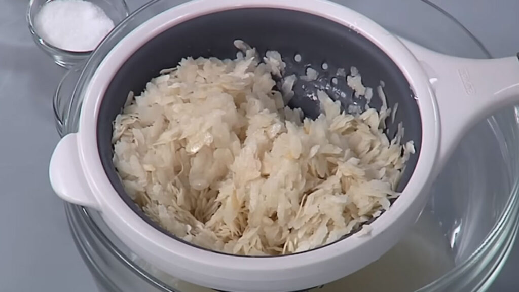 Flattened rice (poha) being rinsed in a bowl of water to soften before cooking