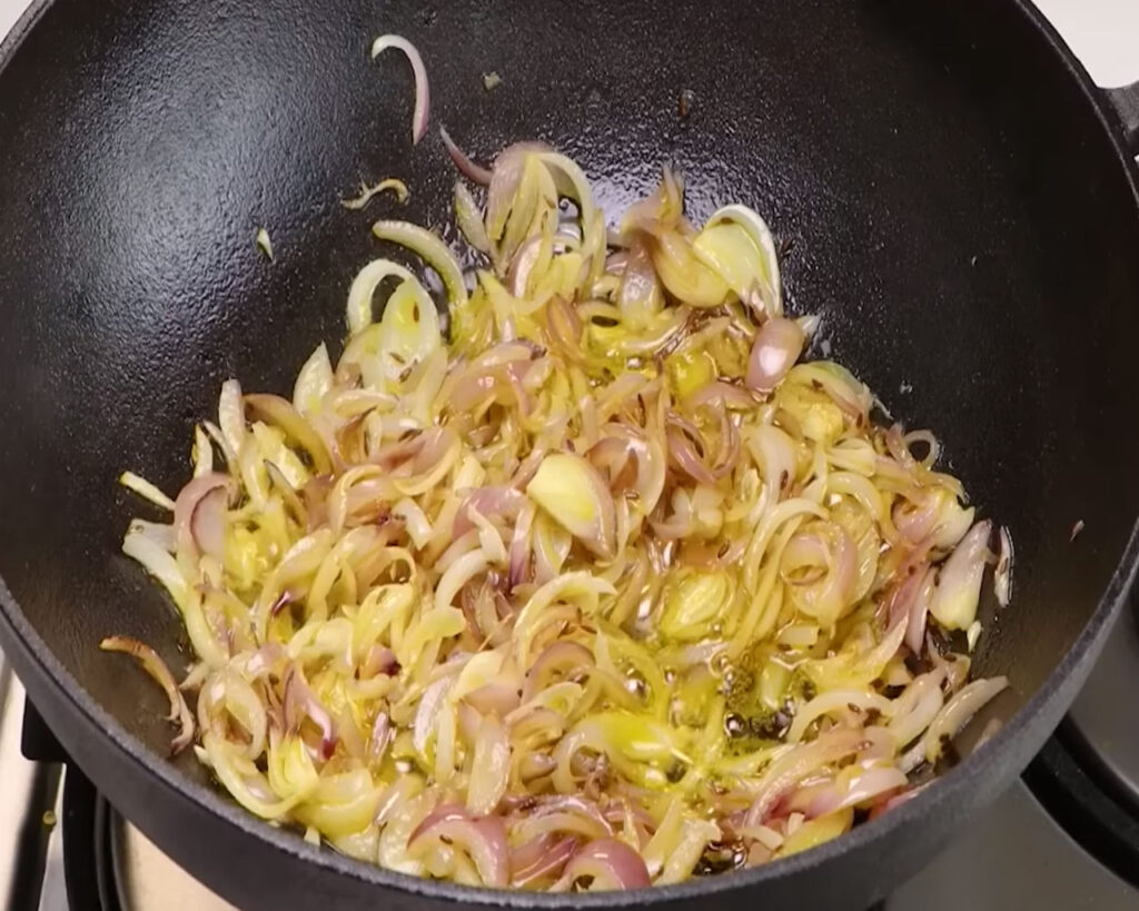 Finely chopped onions being sautéed to golden brown in mustard oil for Rajma Masala base.