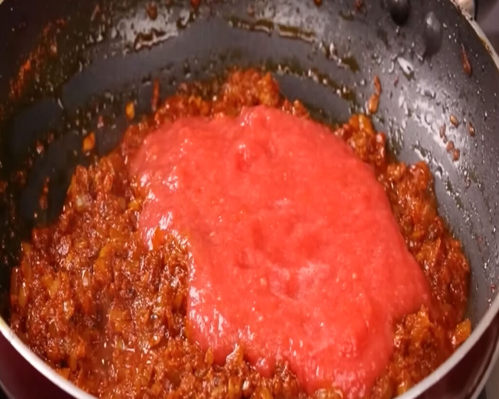 Tomato paste added to the pan with masala paste, simmering on low flame with a lid covered