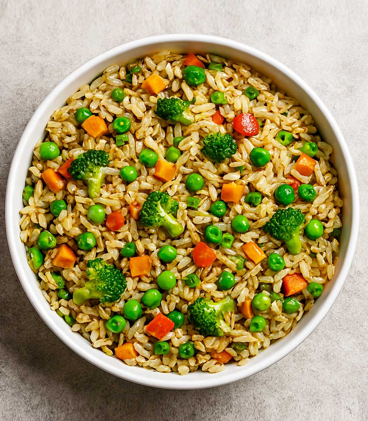 Indian veg fried rice served on a white plate, loaded with colorful vegetables like carrots, beans, and capsicum, garnished with broccoli.