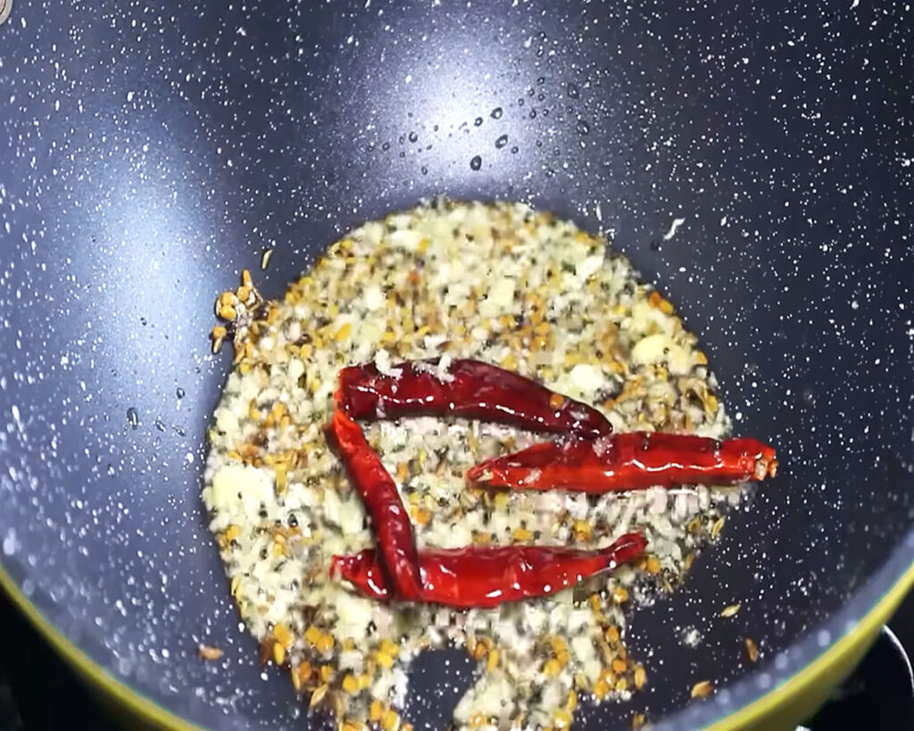 Adding ginger garlic paste to the pan to infuse flavor into the Kadhi.
