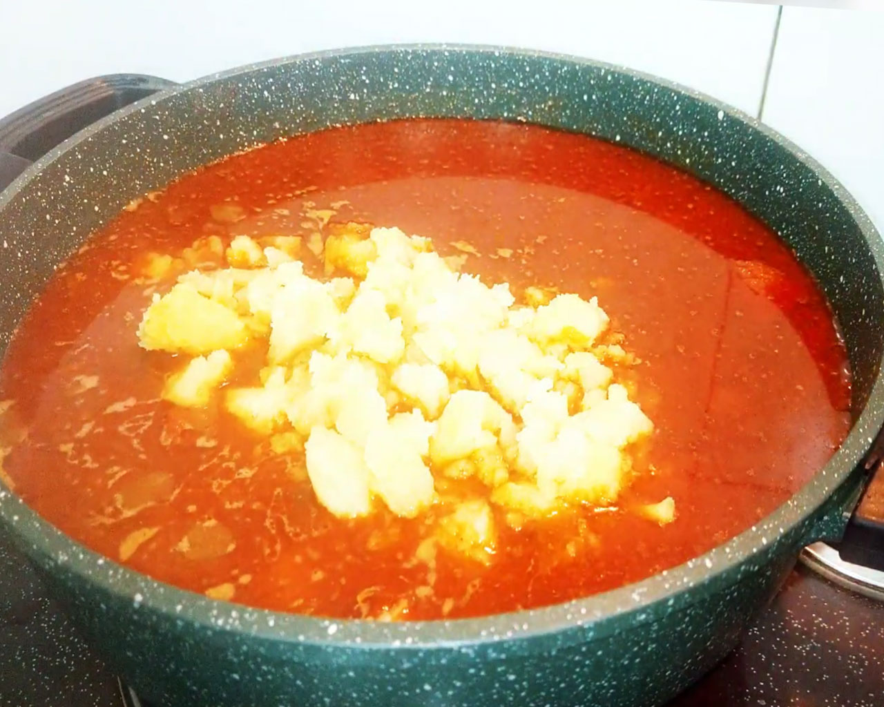 Mashed boiled potatoes being added to chickpea curry