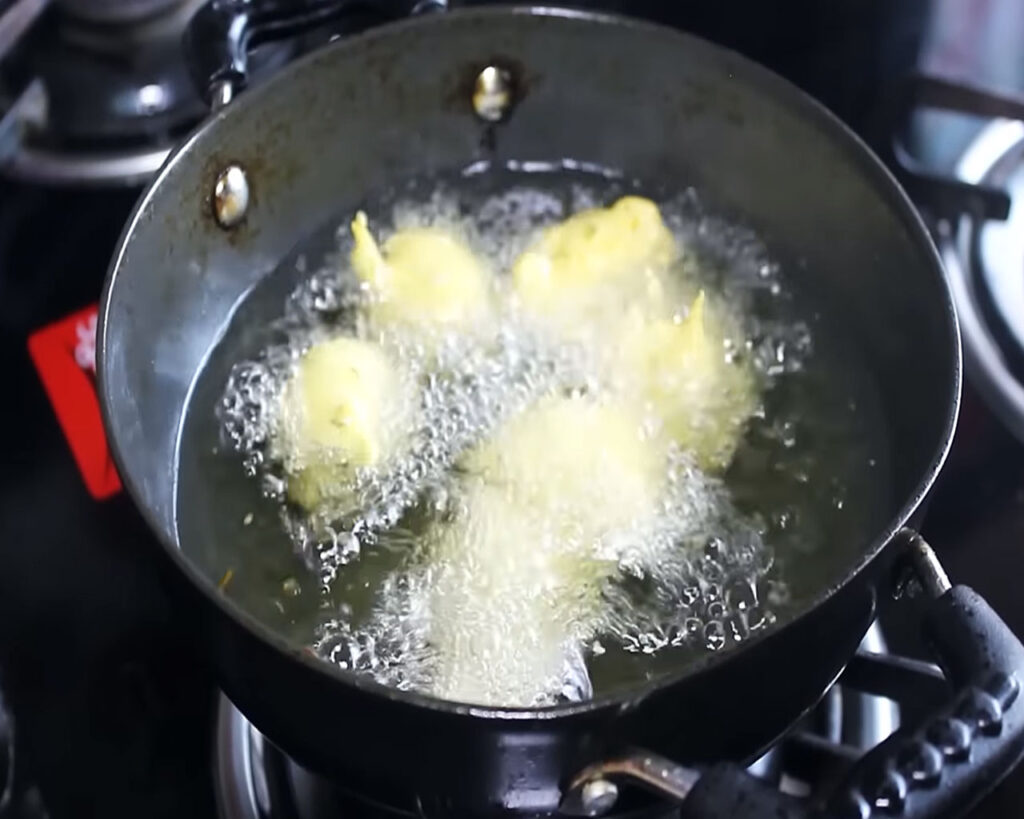 Shaping and frying small balls of Kadhi Pakora batter in hot mustard oil.