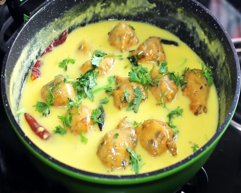 Garnishing Kadhi Pakora with chopped coriander leaves before serving.