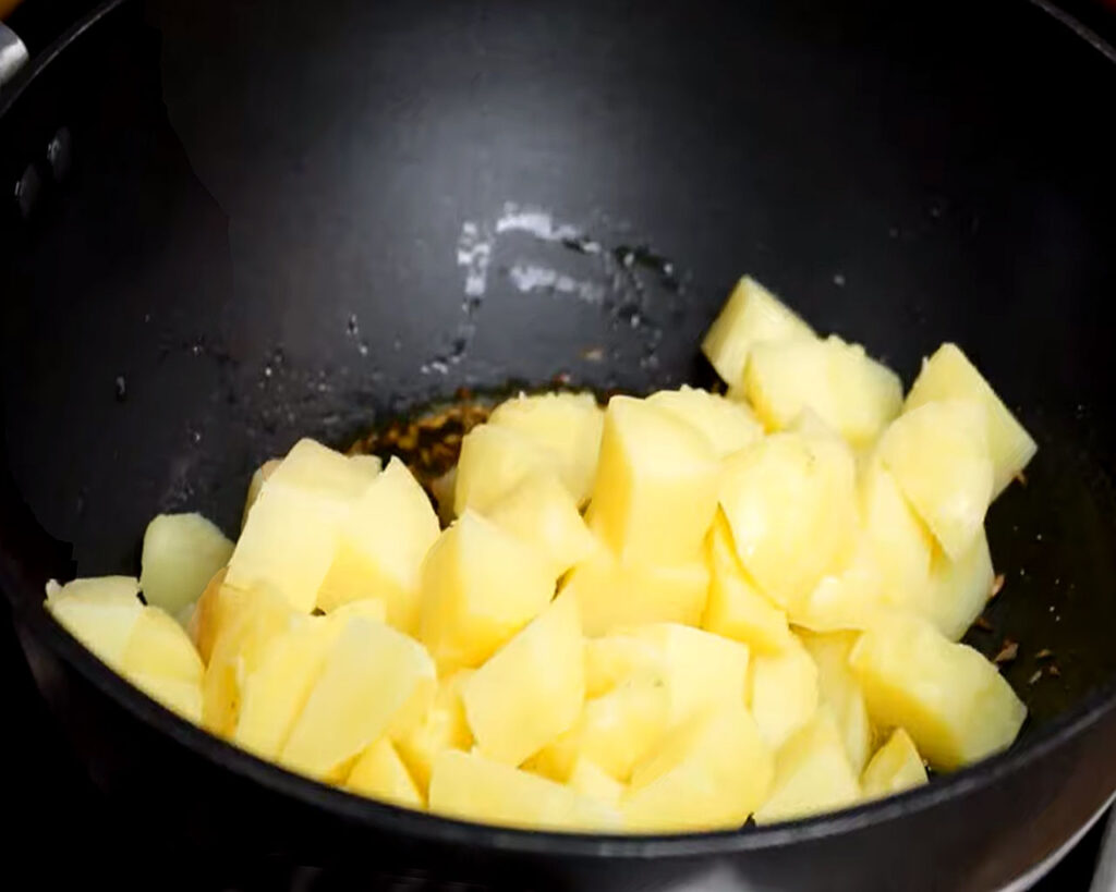 Adding boiled and cubed potatoes to the pan to make Jeera Aloo