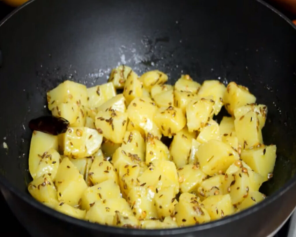 Mixing potatoes with the tadka for Jeera Aloo.