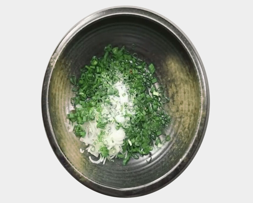 Bowl with ginger, chopped spring onions, black pepper, and soy sauce being mixed with a spoon