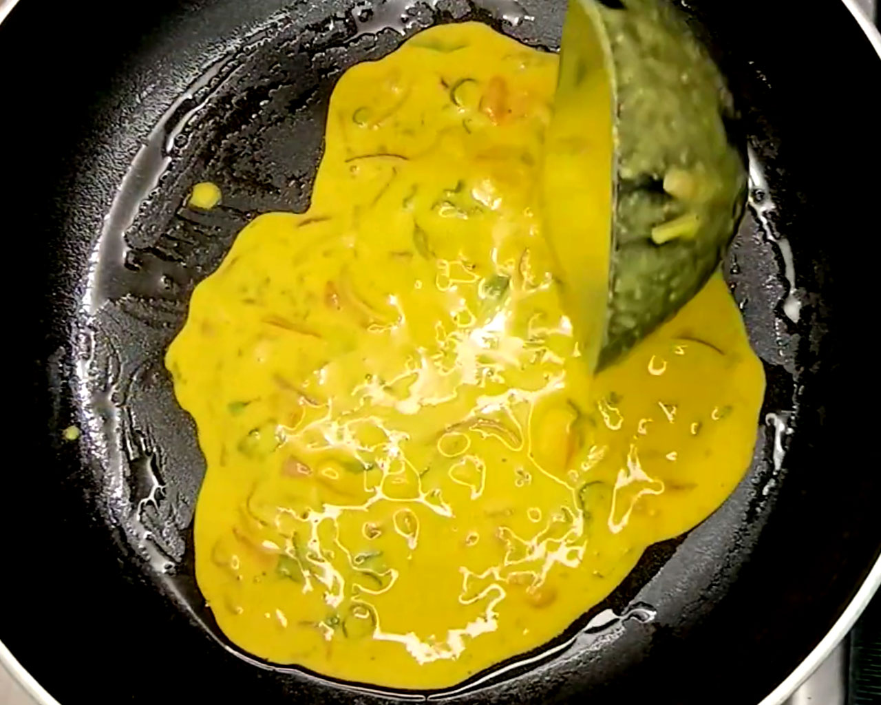 Pouring chilla batter into the pan and spreading it in a circular motion.