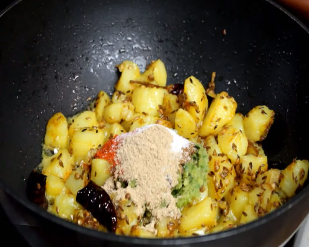 Adding spices like turmeric, red chili powder, and garam masala to enhance the flavor of Jeera Aloo