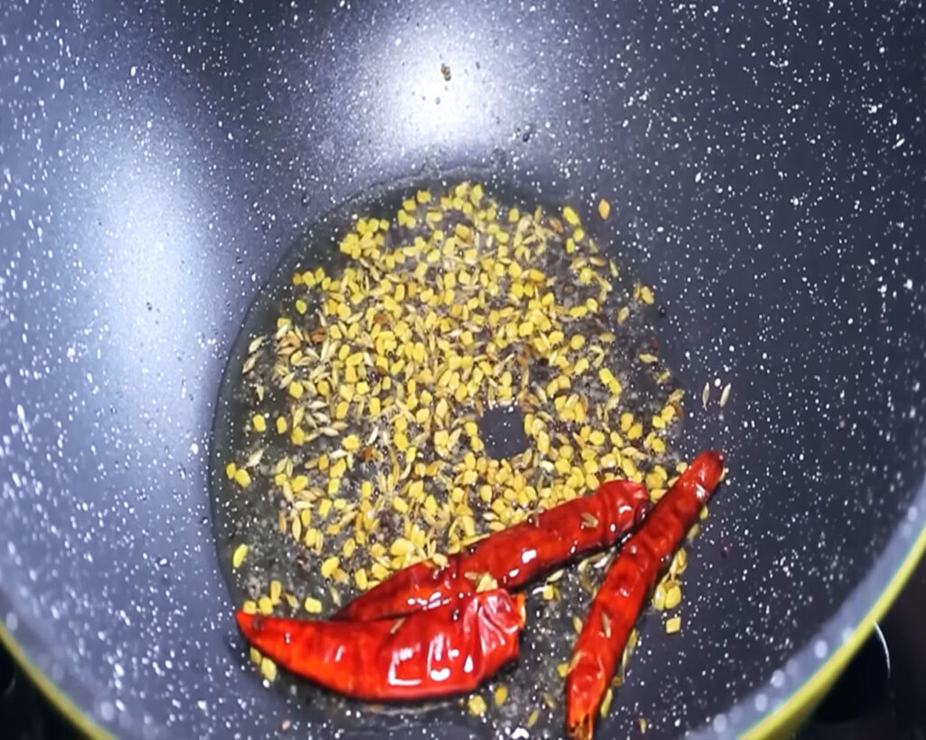Sautéing mustard seeds, cumin seeds, and dried red chilies for Kadhi Pakora tempering.