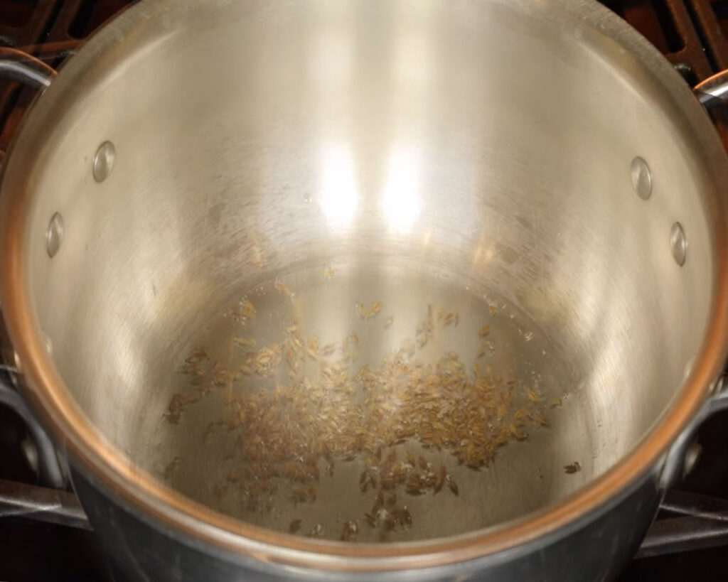 Cumin seeds sizzling in hot oil in a wok to start cauliflower curry recipe
