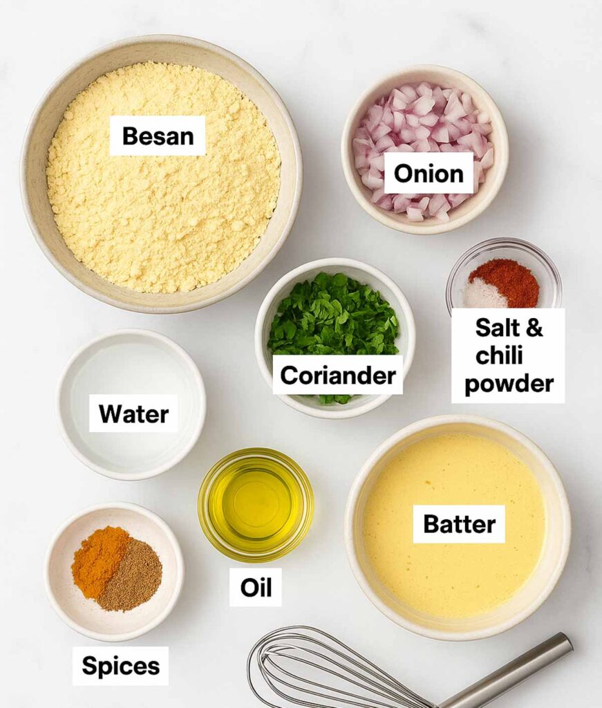 Ingredients for Besan Chilla recipe neatly arranged on a kitchen rack, gram flour, onions, tomatoes, green chilies, spices, and herbs in bowls.