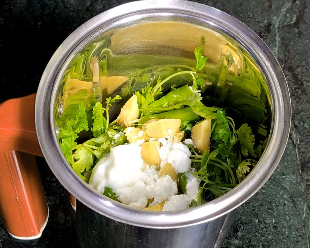 Blender filled with coconut pieces, roasted chana dal, peanuts, coriander, green chilies, curd and water for chutney preparation