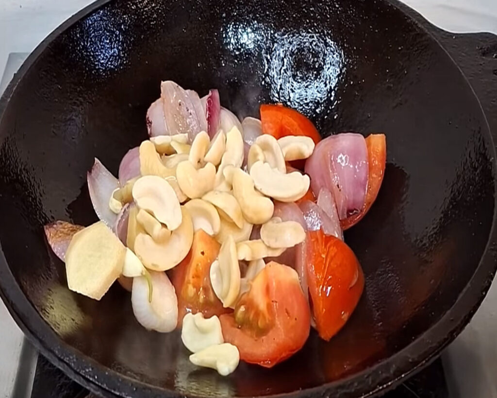 Tomatoes, ginger, garlic, and cashews cooking in a pan for curry paste