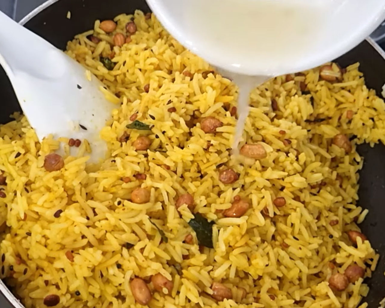 Fresh lemon juice being poured over cooked rice to make lemon rice