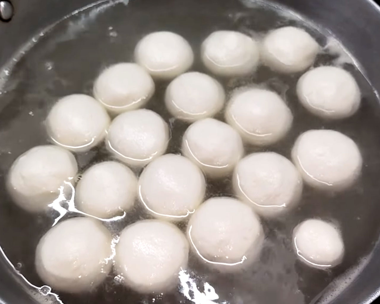 Dropping smooth rasgulla balls carefully into boiling sugar syrup.
