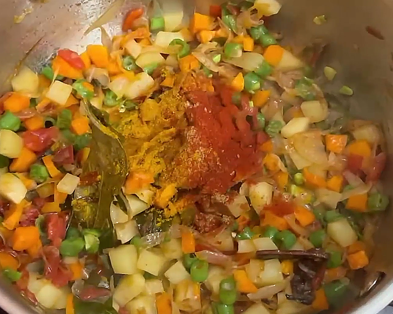 Red chili powder, coriander powder, and garam masala being sprinkled over mixed vegetables in the pot for veg kurma