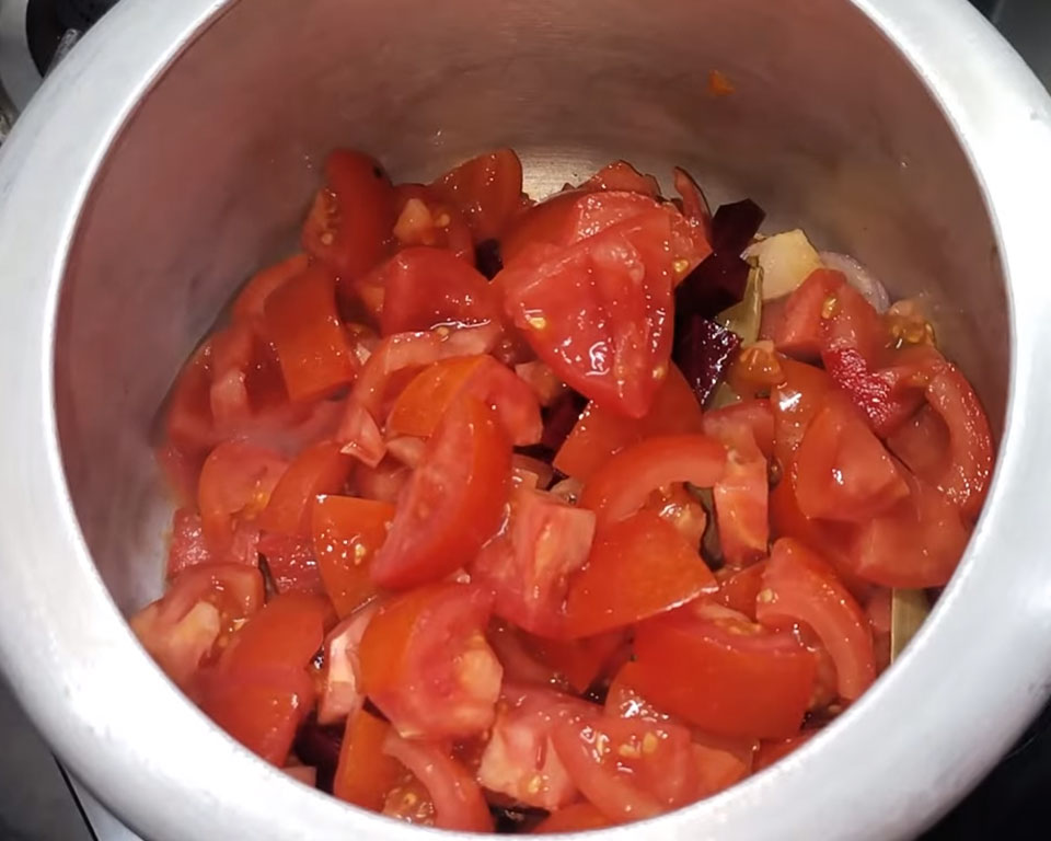 Adding diced tomatoes and chopped beetroot into the pressure cooker for homemade Indian tomato soup.